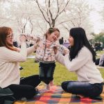 a group of women sitting on top of a blanket in a park