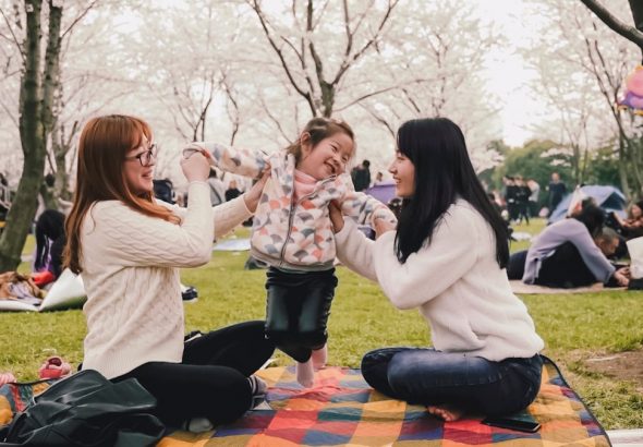a group of women sitting on top of a blanket in a park