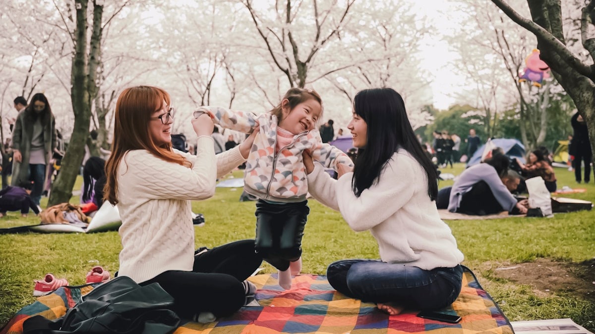 a group of women sitting on top of a blanket in a park